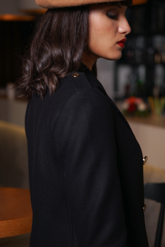 Détails du manteau noir avec boutons traditionnels.