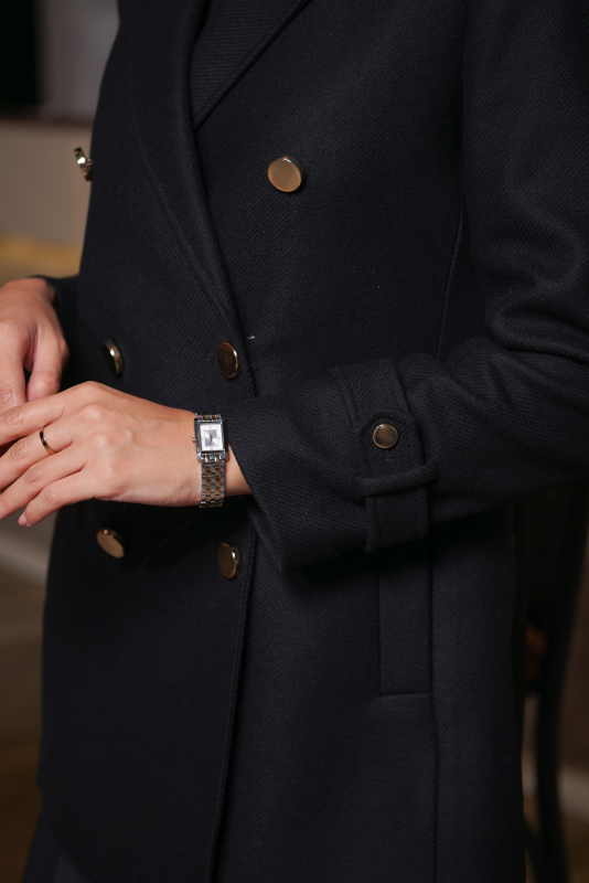 Détails du manteau noir avec boutons traditionnels.