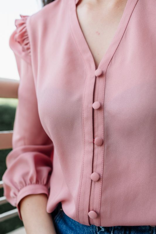 Détails de la blouse en rose : manches longues et petits boutons.