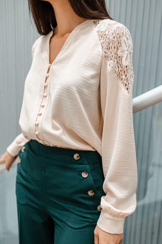 Blouse beige de couleur douce pour femme sur un fond neutre.