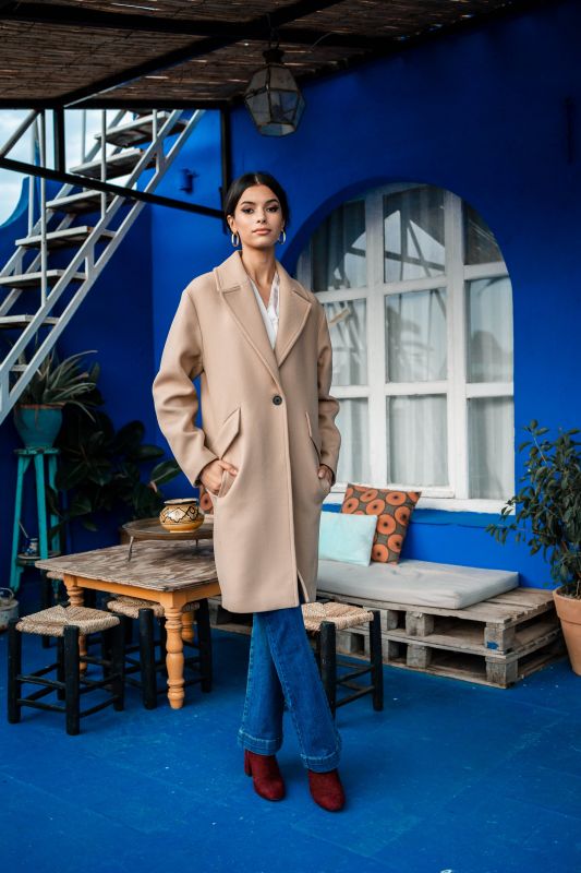Manteau de couleur beige, rehaussé par un bouton discret.