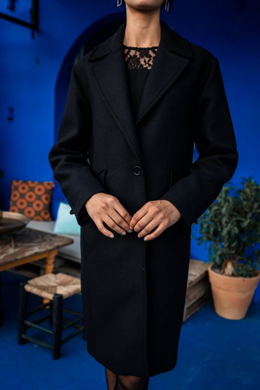 Manteau noir avec un bouton discret, élégance subtile.