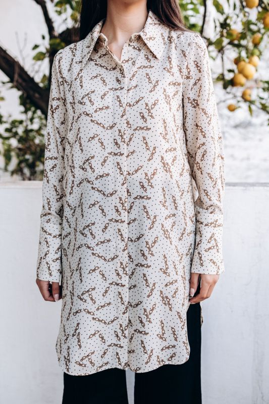 Tunique Oum à motif chaîne sur fond blanc, collection Ramadan Vibes d'ANAE, portée dans un cadre verdoyant.
