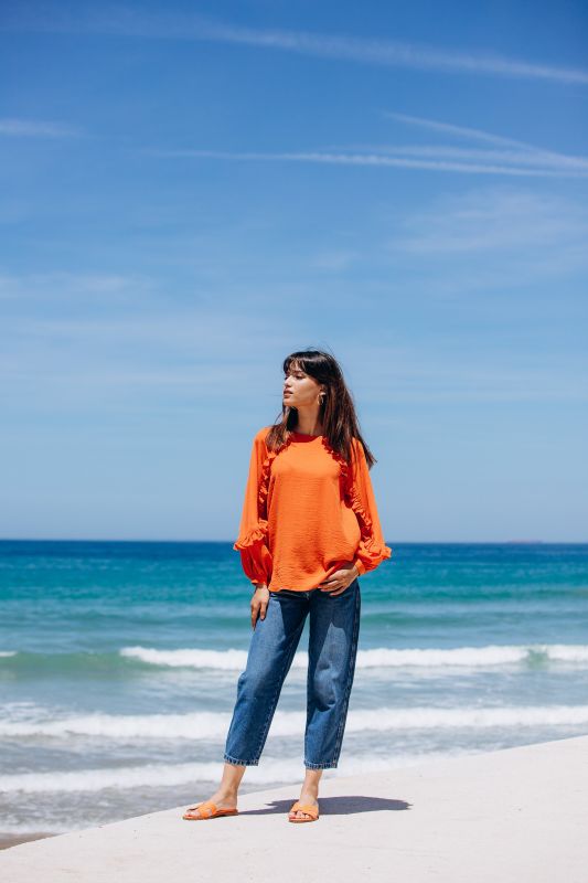 portant une blouse orange à la plage.