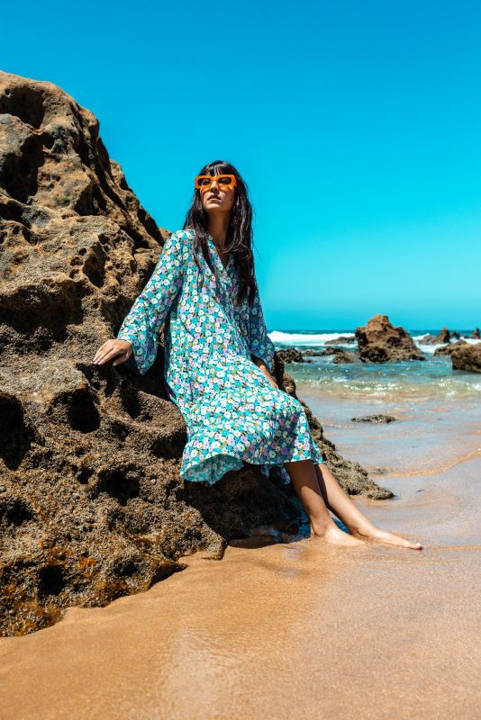 Robe longue Frances à motif floral, femme posant sur un rocher en bord de mer.