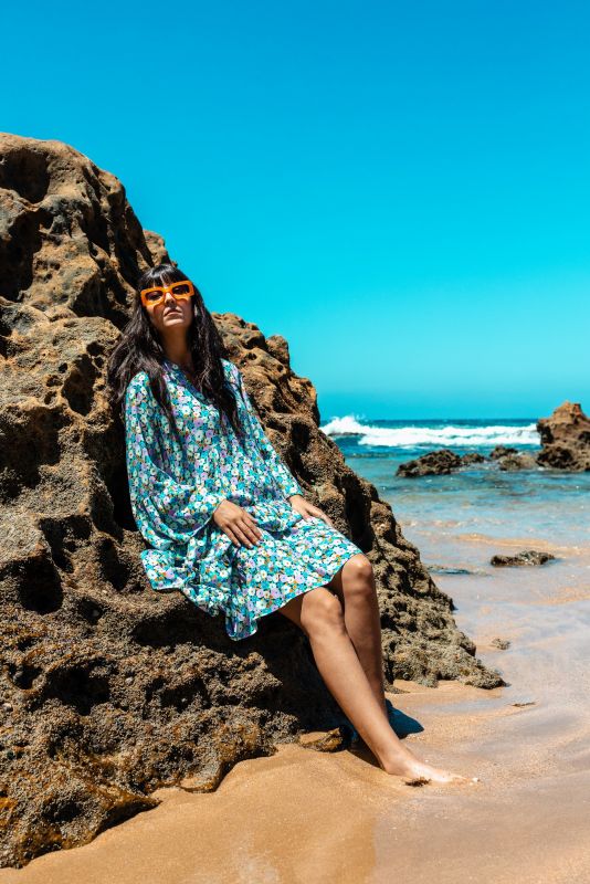 Robe longue Frances à motif floral, femme posant sur un rocher en bord de mer.