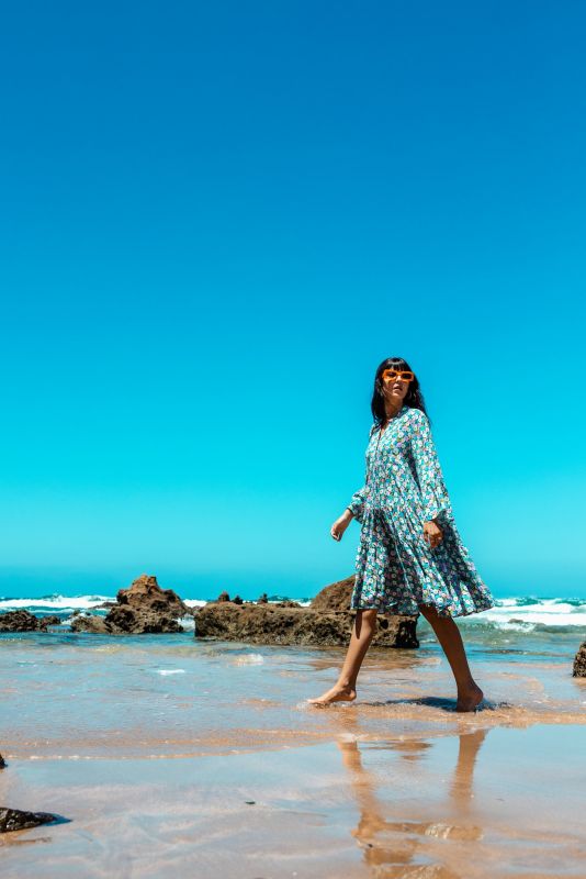 Robe longue Frances à motif floral, femme posant sur un rocher en bord de mer.