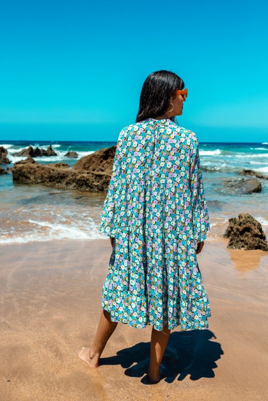 Femme tenant élégamment le tissu de sa robe Frances fleurie d'ANAE, reflétant un style bohème.