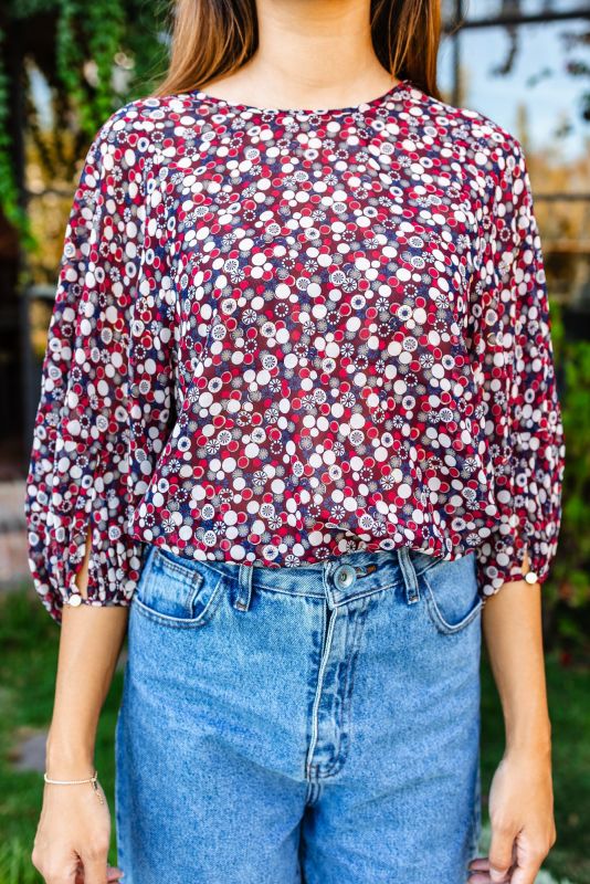 Gros plan d'une femme portant une blouse rouge à motifs floraux et un jean bleu clair, mettant l'accent sur la blouse.