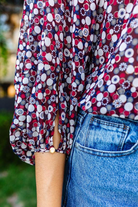 Gros plan d'une femme portant une blouse rouge à motifs floraux et un jean bleu clair, mettant l'accent sur la blouse.