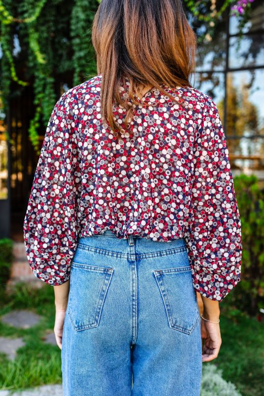 Vue rapprochée de côté d'une femme portant une blouse rouge à motifs floraux, mettant en évidence le détail de la manche.