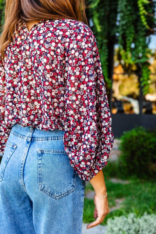 Vue rapprochée de côté d'une femme portant une blouse rouge à motifs floraux, mettant en évidence le détail de la manche.
