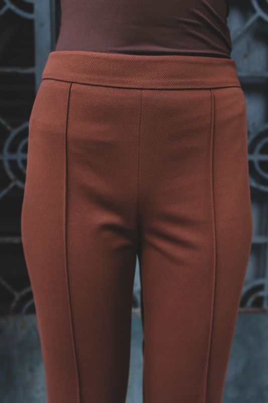 Détail du pantalon Harold brun texturé, collection Checks d'ANAE, sur fond urbain métallique.