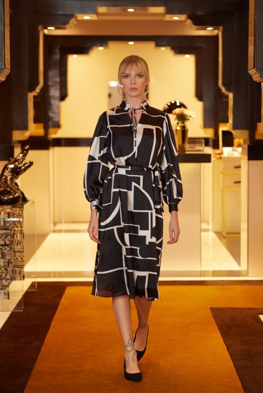 Femme élégante portant la ROBE DELILAH en noir et blanc de la collection FIESTA 24 d'ANAE, devant un décor luxueux.
