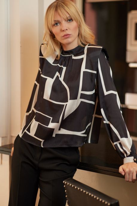 Femme en blouse Christy d'ANAE, motif géométrique noir et blanc, élégance contemporaine pour un look professionnel.