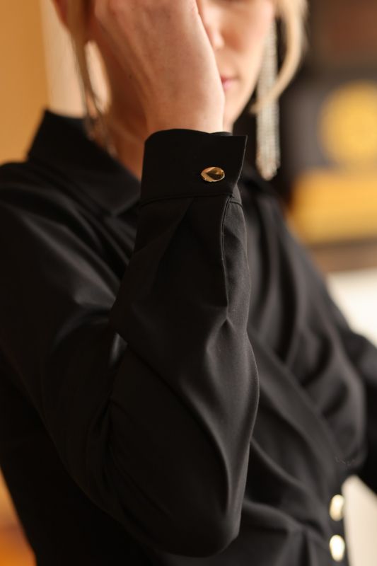 La blouse croisée May d'ANAE, avec ses boutons dorés, offre une touche de luxe à cette tenue noire épurée.