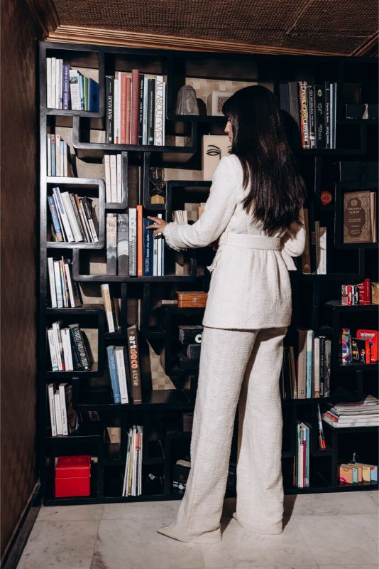 Élégante femme assise dans un fauteuil vintage, portant un pantalon de tweed blanc ANAE, évoquant détente et sophistication.