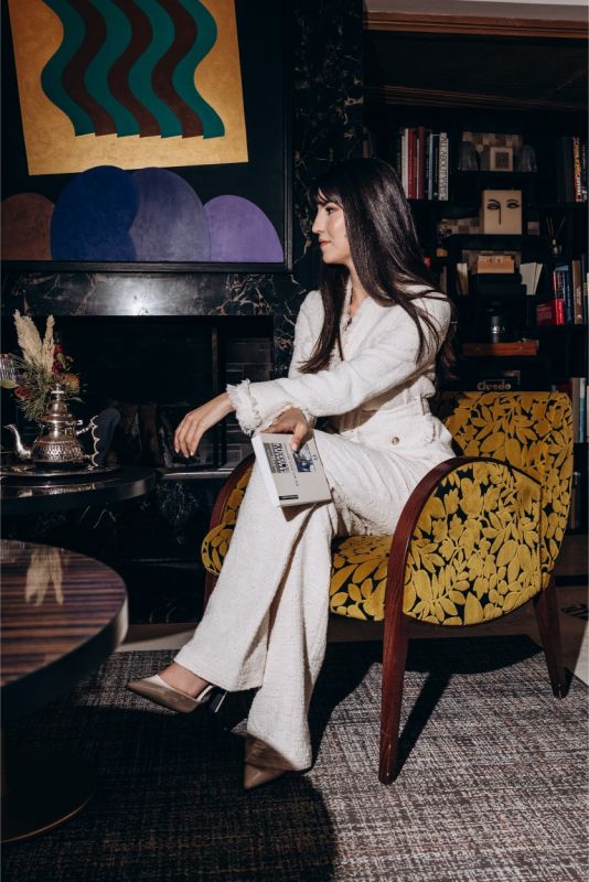 Élégante femme assise dans un fauteuil vintage, portant un pantalon de tweed blanc ANAE, évoquant détente et sophistication.