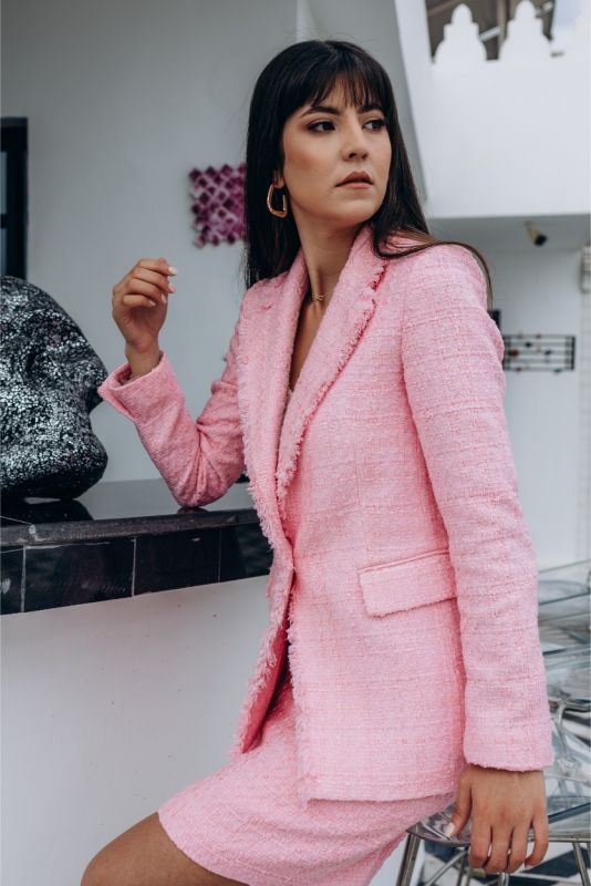 Femme élégante en veste et jupe en tweed rose ANAE, posant sur un toit urbain, parfaite harmonie de style et confort.