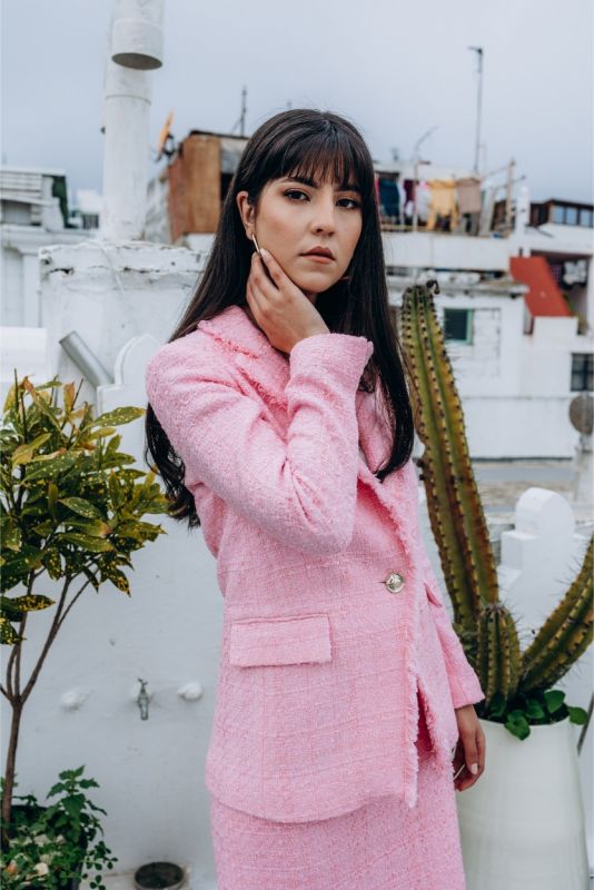 Femme élégante en veste et jupe en tweed rose ANAE, posant sur un toit urbain, parfaite harmonie de style et confort.