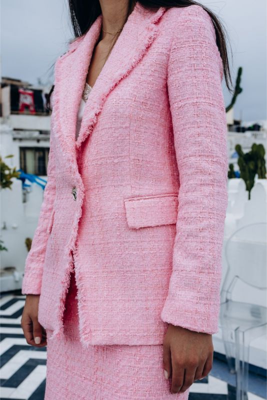 Gros plan sur une veste en tweed rose avec finition effilochée et bouton doré, signe d'élégance discrète.