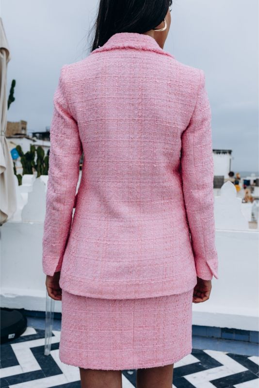 Gros plan sur une veste en tweed rose avec finition effilochée et bouton doré, signe d'élégance discrète.