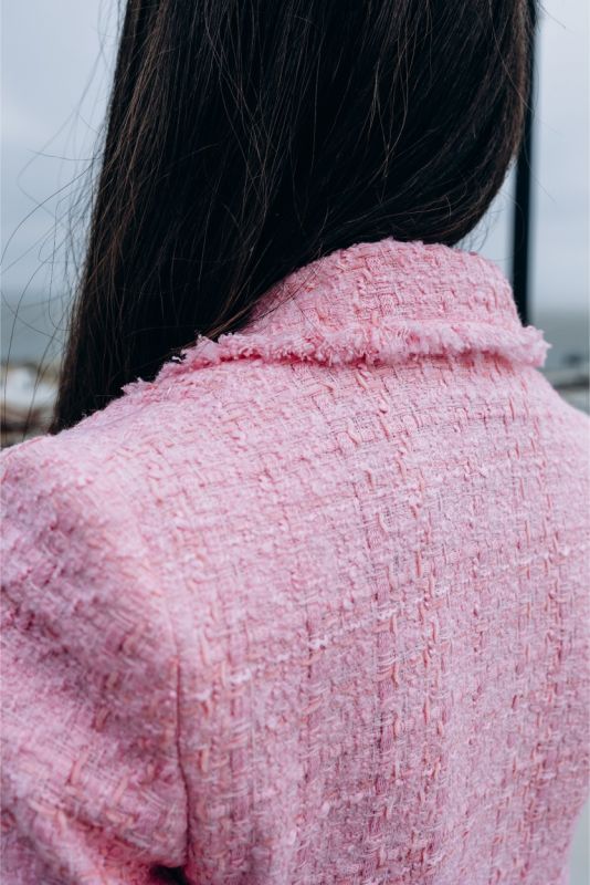 Femme élégante en veste et jupe en tweed rose ANAE, posant sur un toit urbain, parfaite harmonie de style et confort.