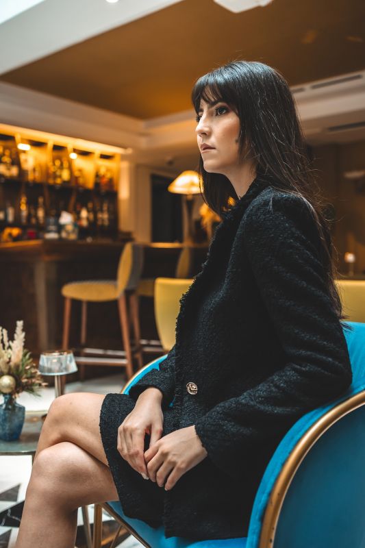 Femme debout avec une veste et jupe tweed Rosy d'ANAE, un ensemble parfait pour un look professionnel et tendance.