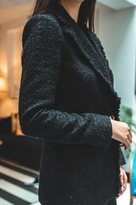 Gros plan sur le tweed noir de la veste ALISIA TWEED 24 d'ANAE, mettant en évidence la qualité du tissu et le bouton détaillé.