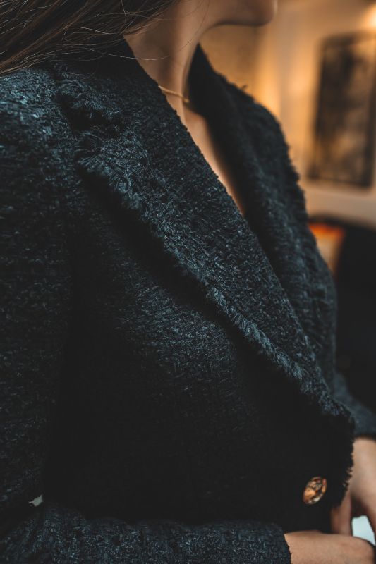 Gros plan sur le tweed noir de la veste ALISIA TWEED 24 d'ANAE, mettant en évidence la qualité du tissu et le bouton détaillé.