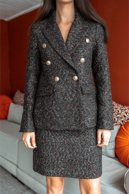 Femme élégante assise, portant la robe PRECIOUS en tweed noir et blanc d'ANAE, incarnant un style chic et intemporel.