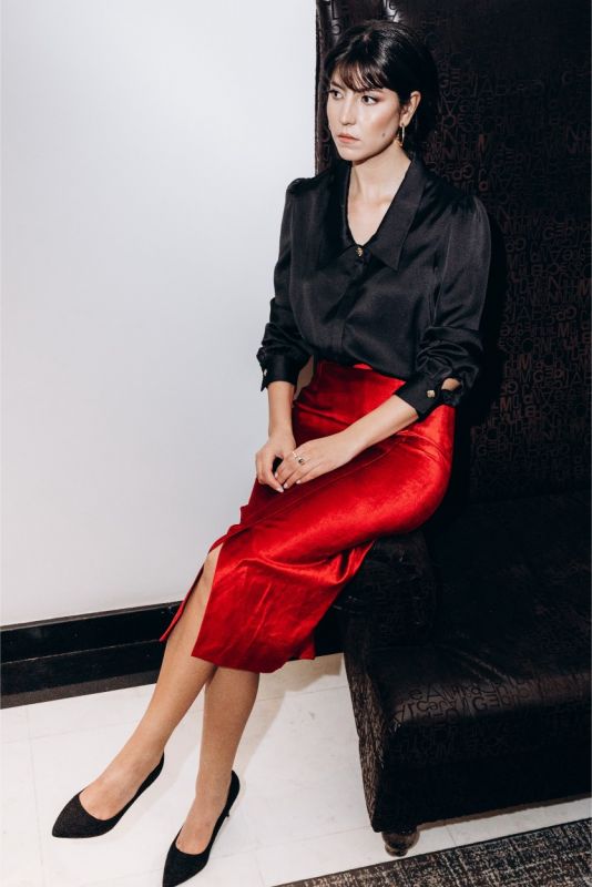 Femme sophistiquée avec une chemise noire ANAE et une jupe en satin rouge, évoquant élégance et style dans un intérieur chic.
