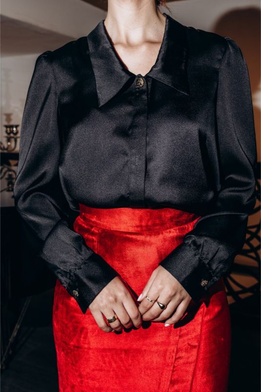Chemise noire décontractée ANAE, détails de boutons bijoux et manchettes ajustées, mariée à une jupe rouge éclatante.