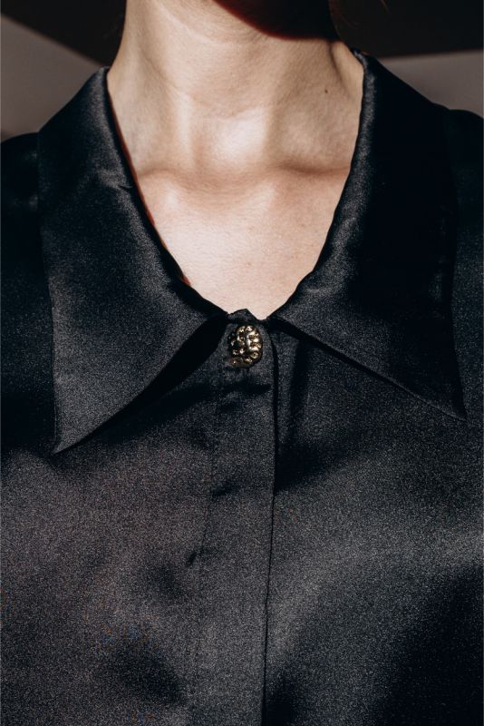 Gros plan sur une chemise noire ANAE avec bouton bijou unique, contrastant superbement avec une jupe rouge satinée.