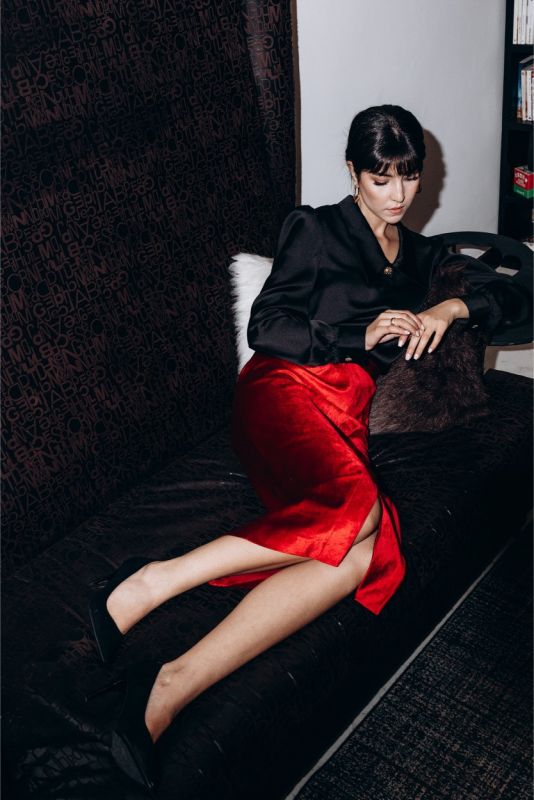 Femme distinguée en jupe rouge satinée BOTERO ANAE et chemise noire, posant dans un intérieur élégant avec des livres d'art.