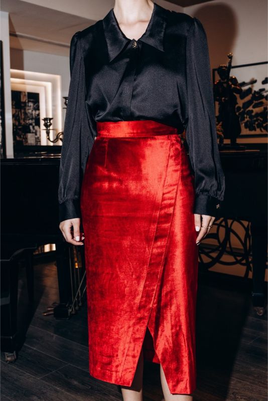 Femme distinguée en jupe rouge satinée BOTERO ANAE et chemise noire, posant dans un intérieur élégant avec des livres d'art.