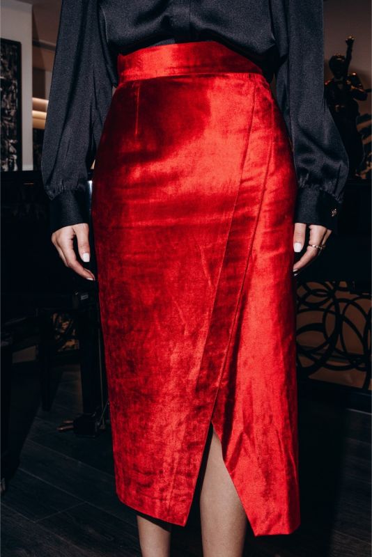Femme distinguée en jupe rouge satinée BOTERO ANAE et chemise noire, posant dans un intérieur élégant avec des livres d'art.