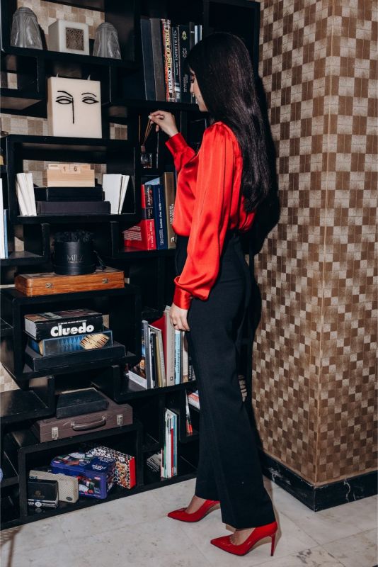 Femme debout dans une bibliothèque, pantalon noir Margaret d'ANAE et chemisier rouge, dégageant une allure professionnelle.
