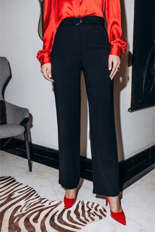 Femme debout dans une bibliothèque, pantalon noir Margaret d'ANAE et chemisier rouge, dégageant une allure professionnelle.
