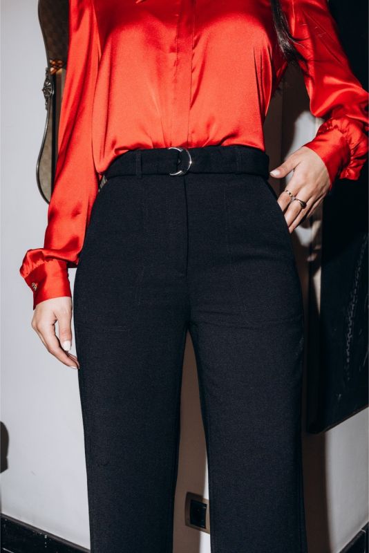 Gros plan sur un pantalon noir ajusté Margaret avec ceinture, porté avec des escarpins rouges pour un contraste audacieux.
