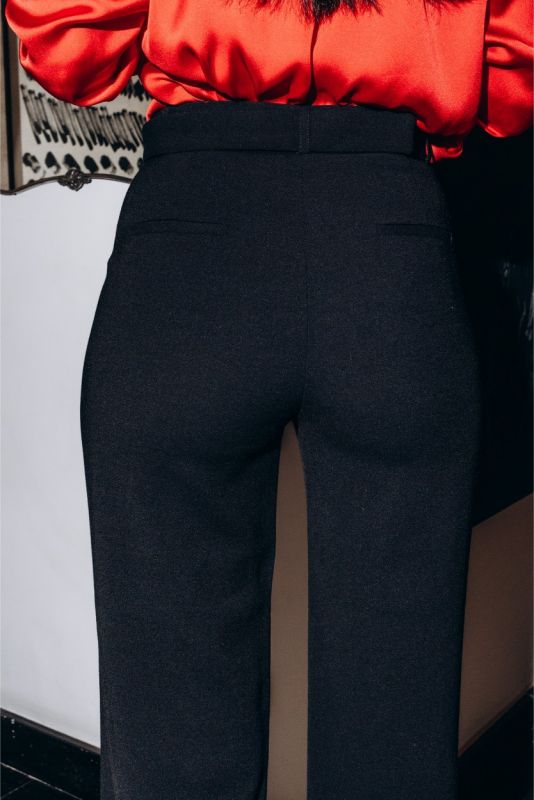 Gros plan sur un pantalon noir ajusté Margaret avec ceinture, porté avec des escarpins rouges pour un contraste audacieux.