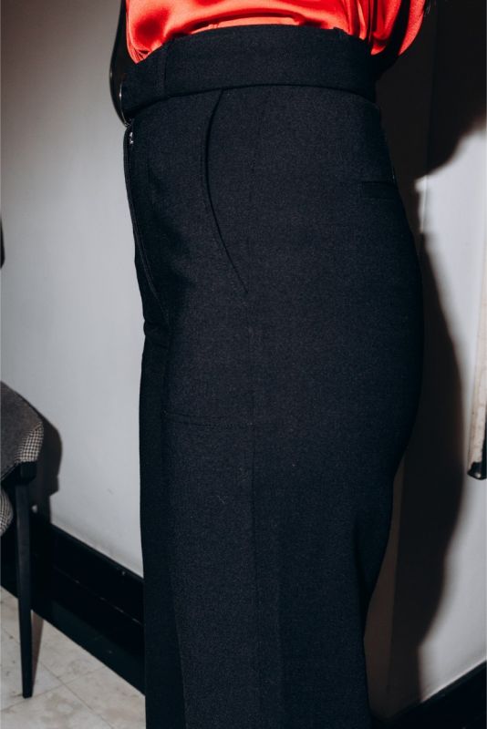 Gros plan sur un pantalon noir ajusté Margaret avec ceinture, porté avec des escarpins rouges pour un contraste audacieux.
