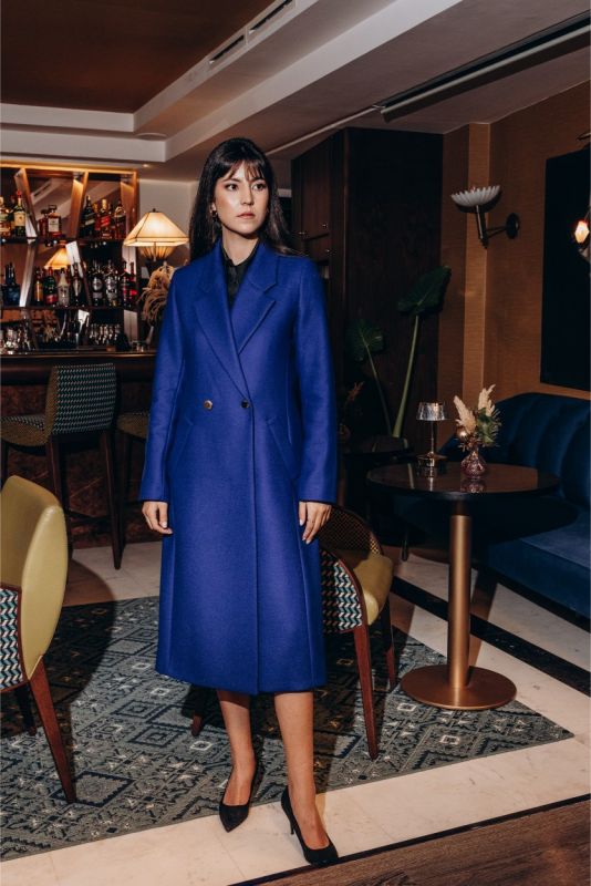 Vue latérale d'une femme portant le manteau Chaouen bleu vibrant d'ANAE, mettant en valeur son design épuré.