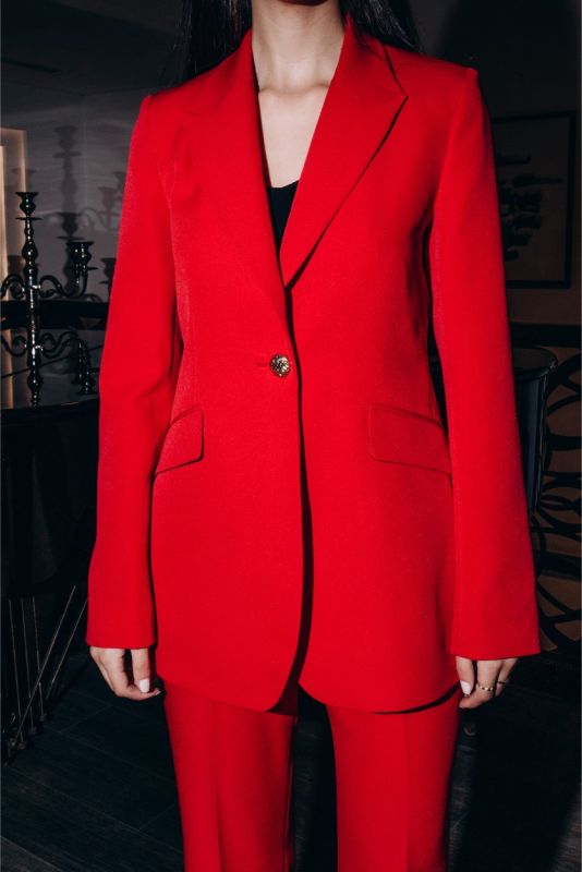 Gros plan sur une veste rouge de tailleur ANAE, bouton détaillé noir et brillant, coupe nette et sophistiquée.