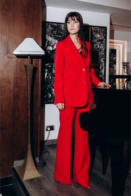 Femme en tenue de travail élégante ANAE, portant un pantalon Tuscany rouge vif et veste assortie, dégageant confiance et style.