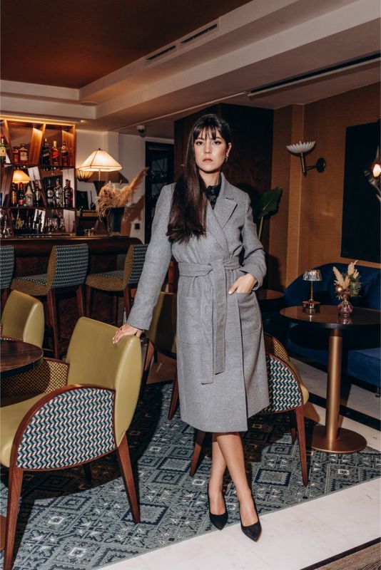 Femme dans un salon moderne portant le manteau Malaga d'ANAE, un choix sophistiqué pour le Nouvel An.