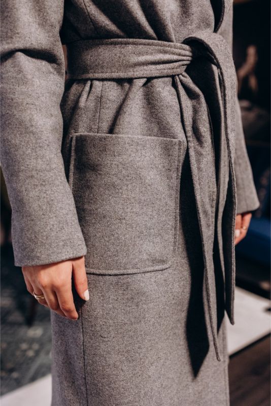 Détail d'un manteau croisé gris ANAE avec une ceinture à nouer, soulignant une coupe ajustée.