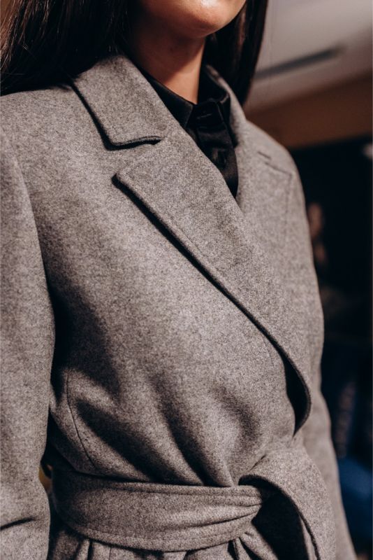 Détail d'un manteau croisé gris ANAE avec une ceinture à nouer, soulignant une coupe ajustée.