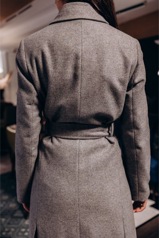 Détail d'un manteau croisé gris ANAE avec une ceinture à nouer, soulignant une coupe ajustée.