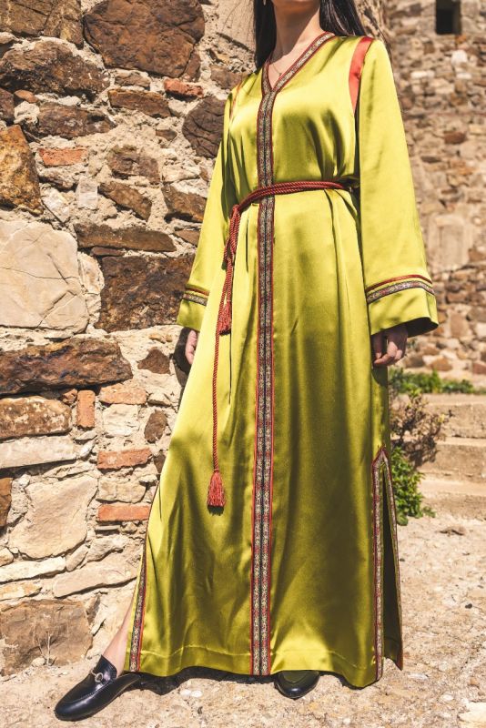 Détail de la bordure rouge et dorée du caftan FAIROUZ d'ANAE sur fond de ruines historiques.